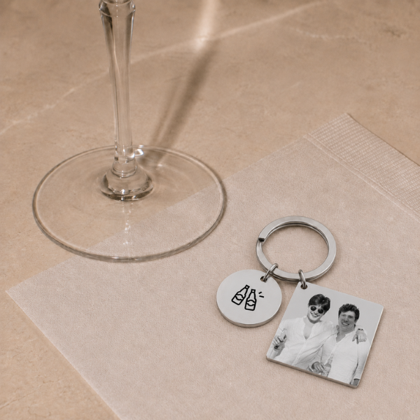Personalisierter silberner Foto-Schlüsselanhänger mit graviertem Kindheitsfoto zweier Jungen und einem runden Anhänger mit der Aufschrift Vom besten Freund zum Trauzeugen, neben einem Champagnerglas
